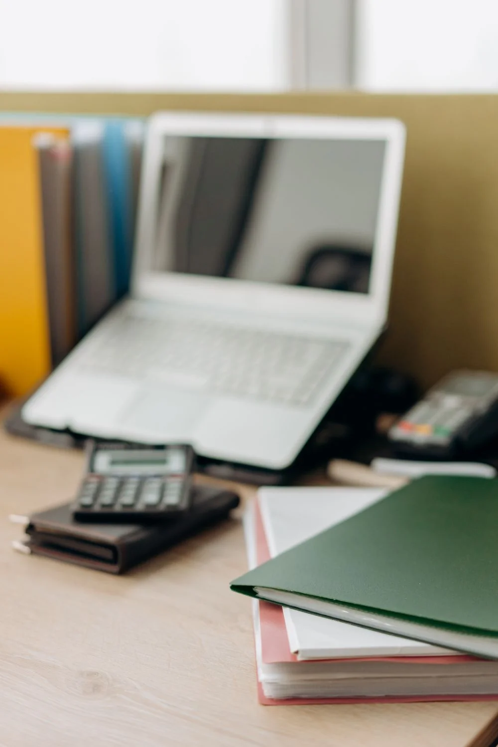 Laptop, calculator and folders on a desk.